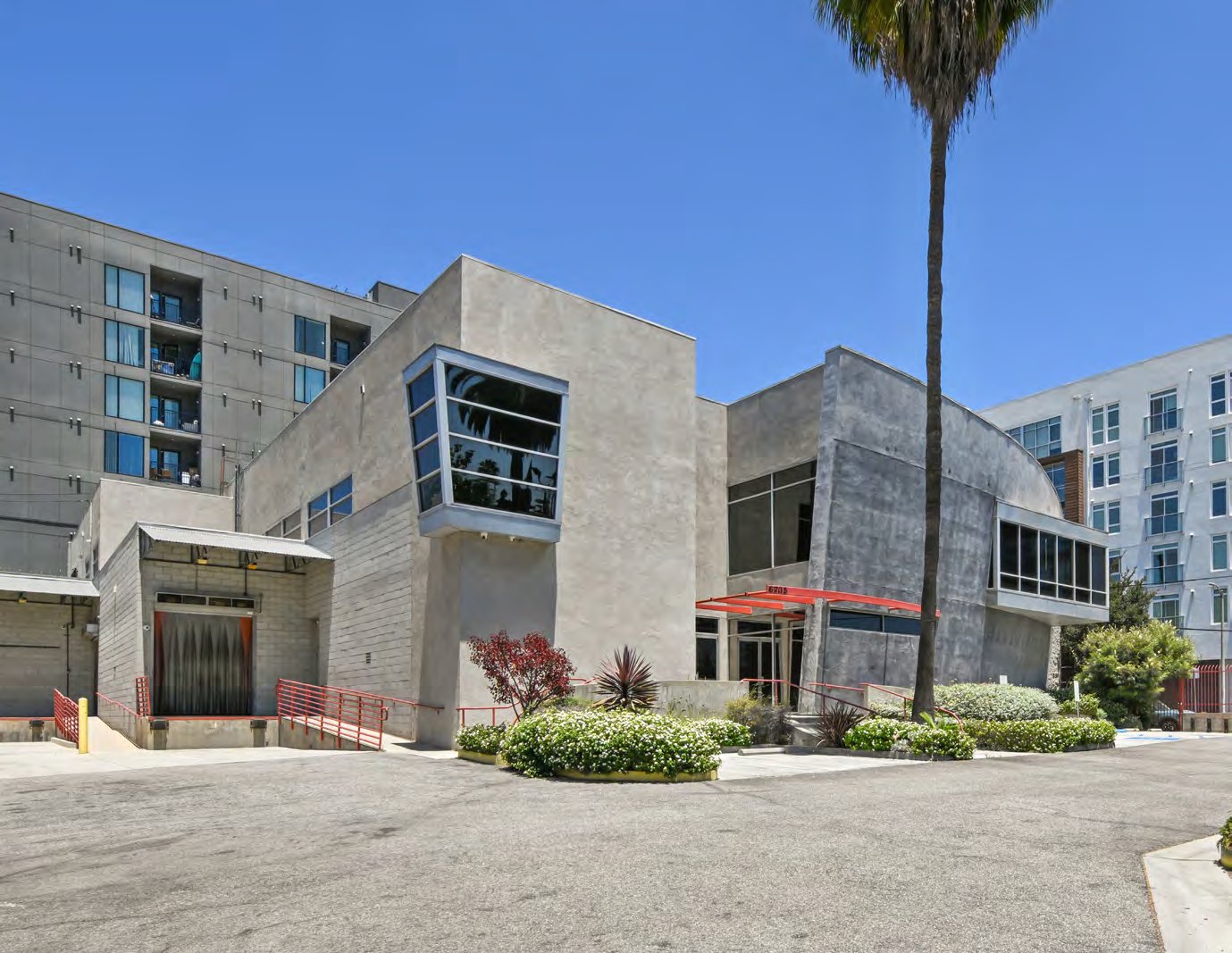 Selma House, a freestanding two-story concrete creative campus at 6735 Selma Avenue in Hollywood, with signature orange-red awnings and a mature palm against a clear sky