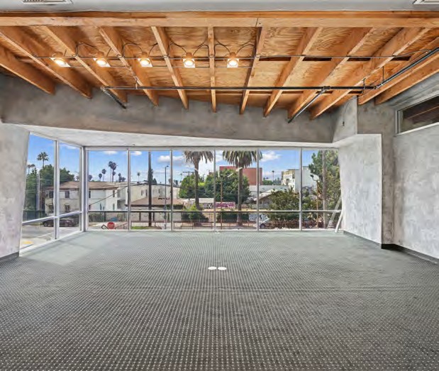 Bright showroom floor with a wood-beam ceiling and full-height windows onto palms