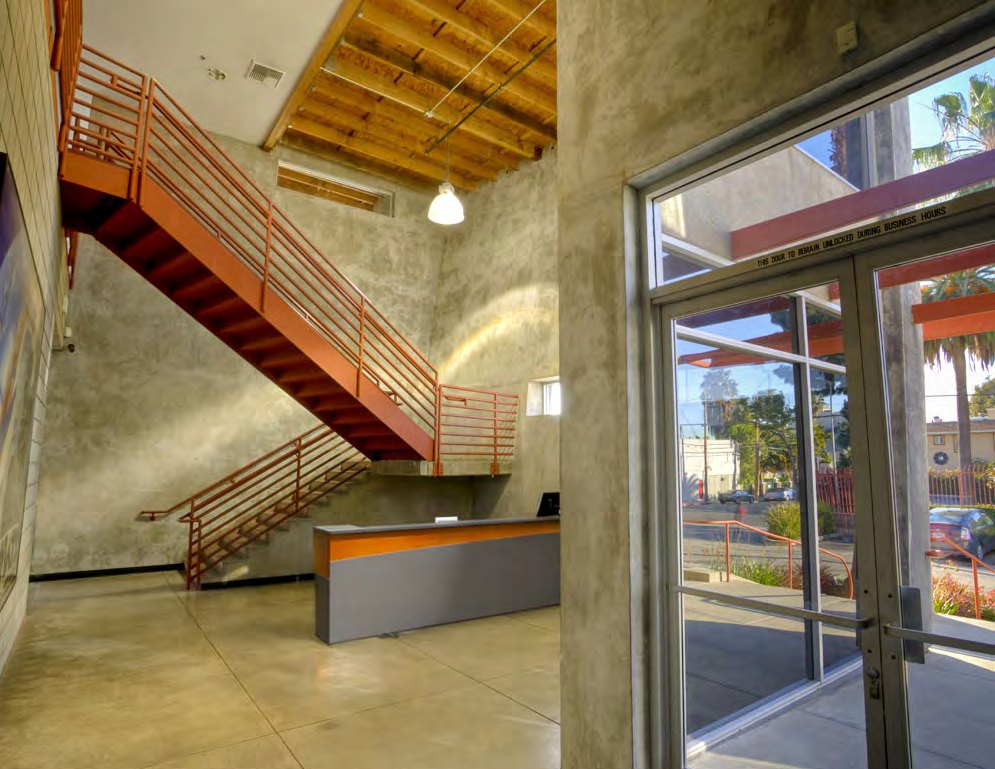 The two-story lobby of Selma House with an exposed orange-red steel stairway, concrete walls, and full-height glass storefront
