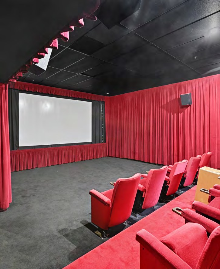The interior screening room and theater at Selma House, with tiered red seating, red side drapery, and a large projection screen